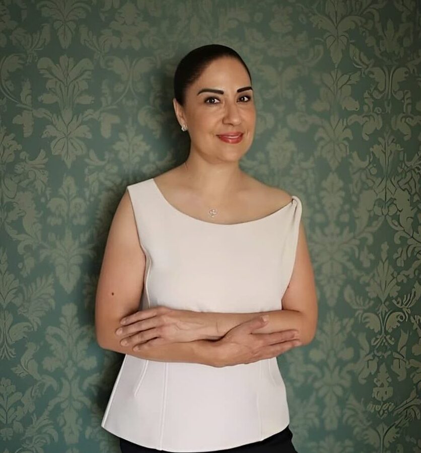 A professional beautician with a warm smile, wearing a white clinic uniform, standing confidently in a modern skincare clinic. Represents qualified expertise at Glow Matrix.