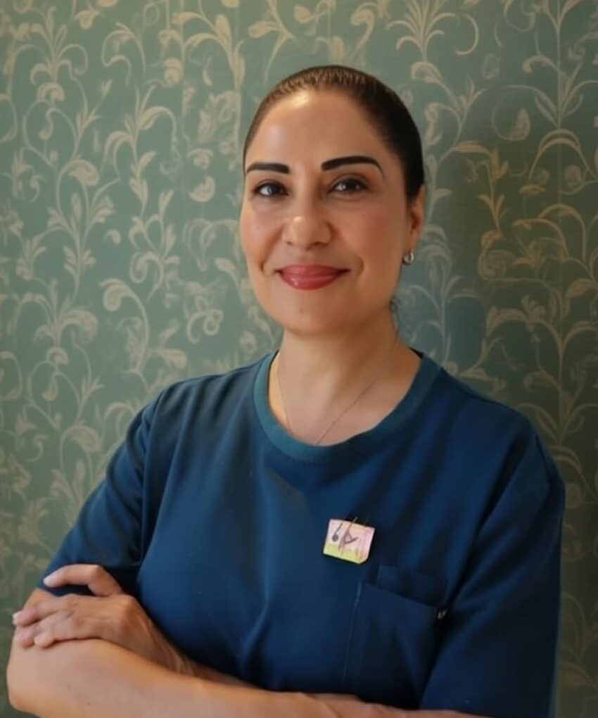 A professional beautician with a warm smile, wearing a white clinic uniform, standing confidently in a modern skincare clinic. Represents qualified expertise at Glow Matrix.