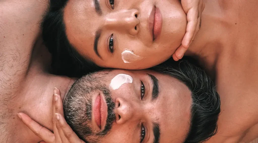 Models posing together with moisturiser visibly applied, radiant dewy skin, faces close together,